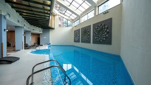 Piscina interior con techo de vidrio transparente, diseño moderno y decoración mural decorativa.