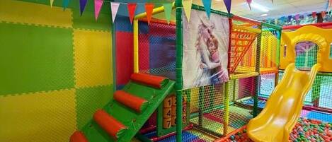 A colorful indoor play area with a slide, soft play surfaces, and a ball pit.