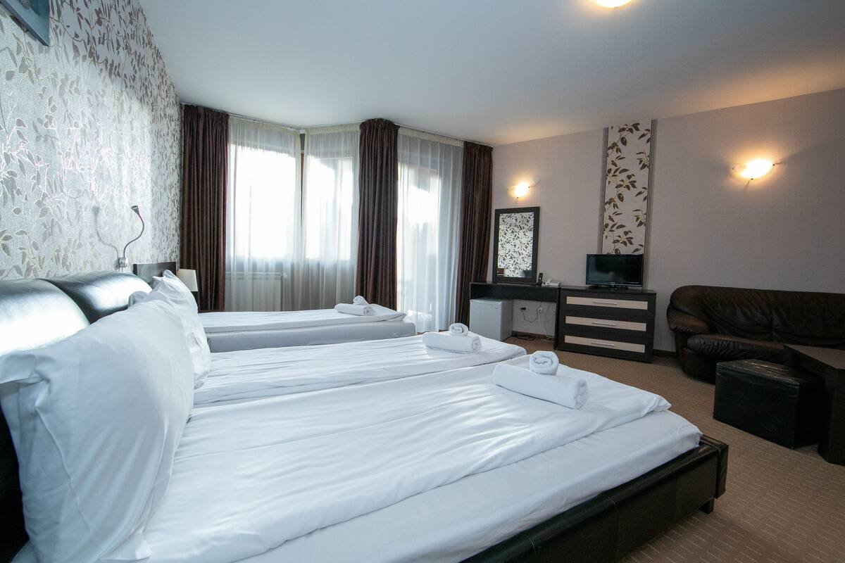 A hotel room with two single beds, a desk, a television, a sofa, and a small cabinet.