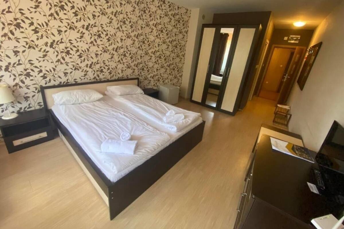 A hotel room with a large bed, a desk with a computer, and a mirror.