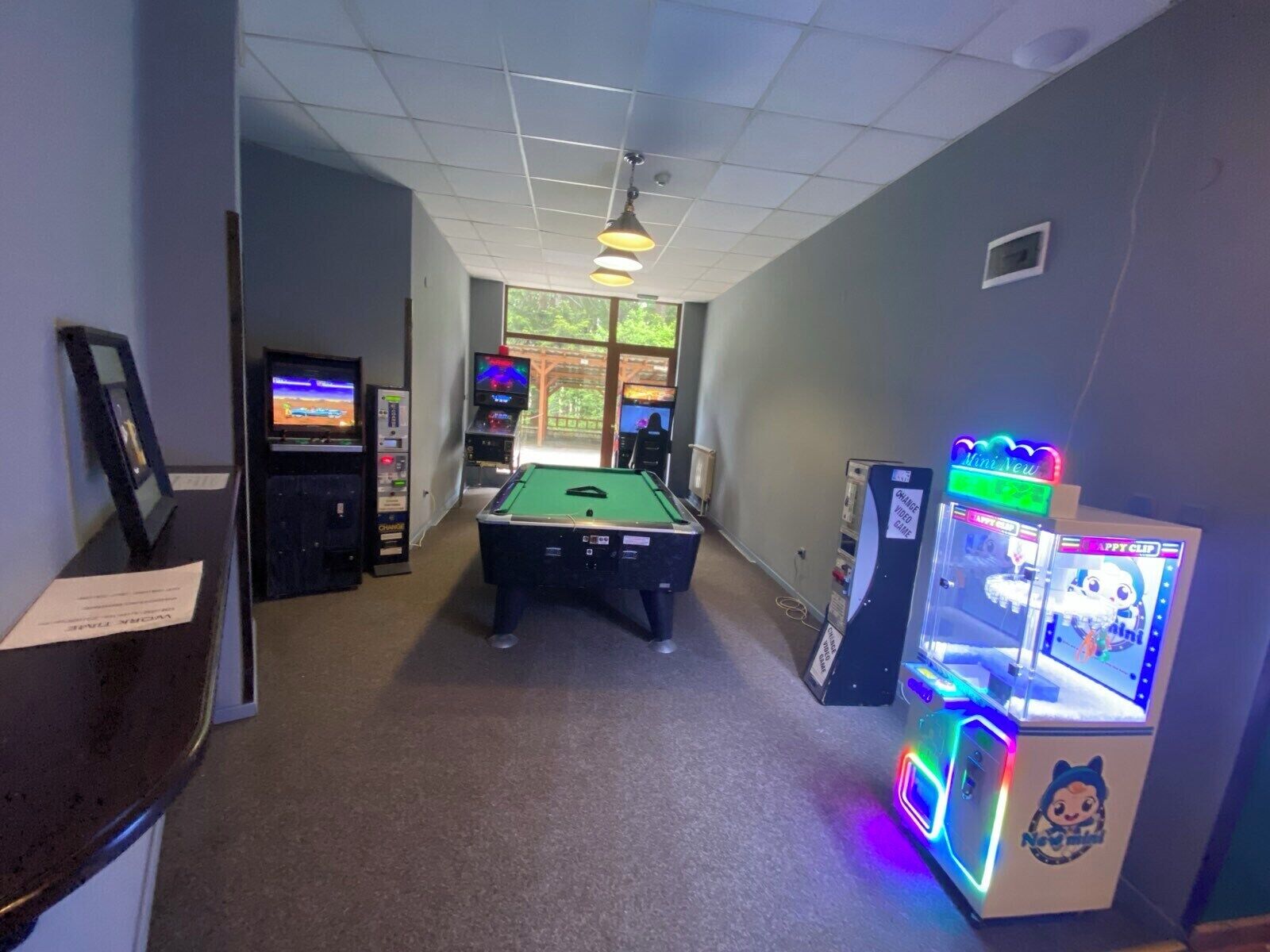 A pool table in a room with arcade games and a large window.