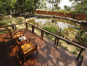 A wooden deck with a table and chairs, overlooking a pond with rocks and plants.