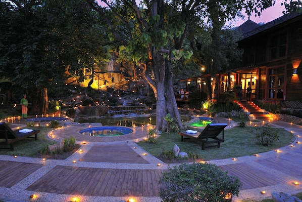 A wooden deck with a pool, surrounded by trees and illuminated by string lights.