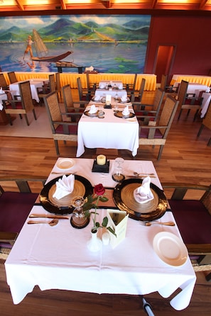 A restaurant with tables set for dining, featuring a mural of a river scene on the wall.