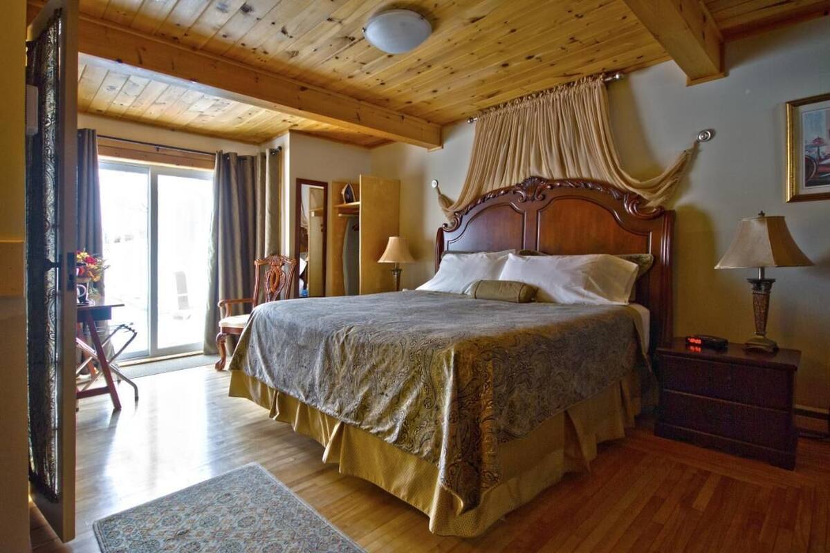 A bedroom with a large bed, wooden ceiling, and a view through a glass door.