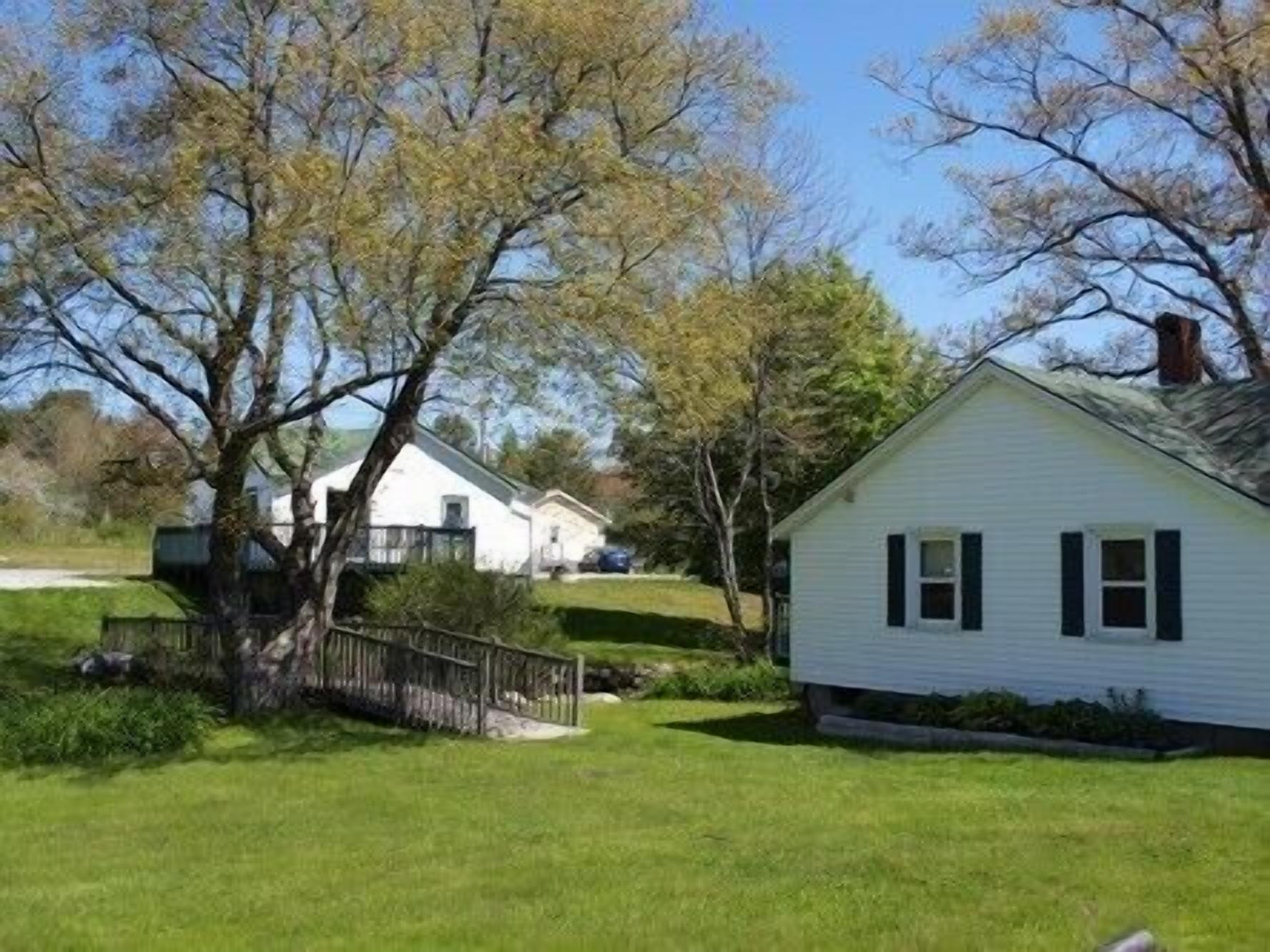 A single-story white house with a gabled roof, surrounded by a well-maintained lawn and mature trees.
