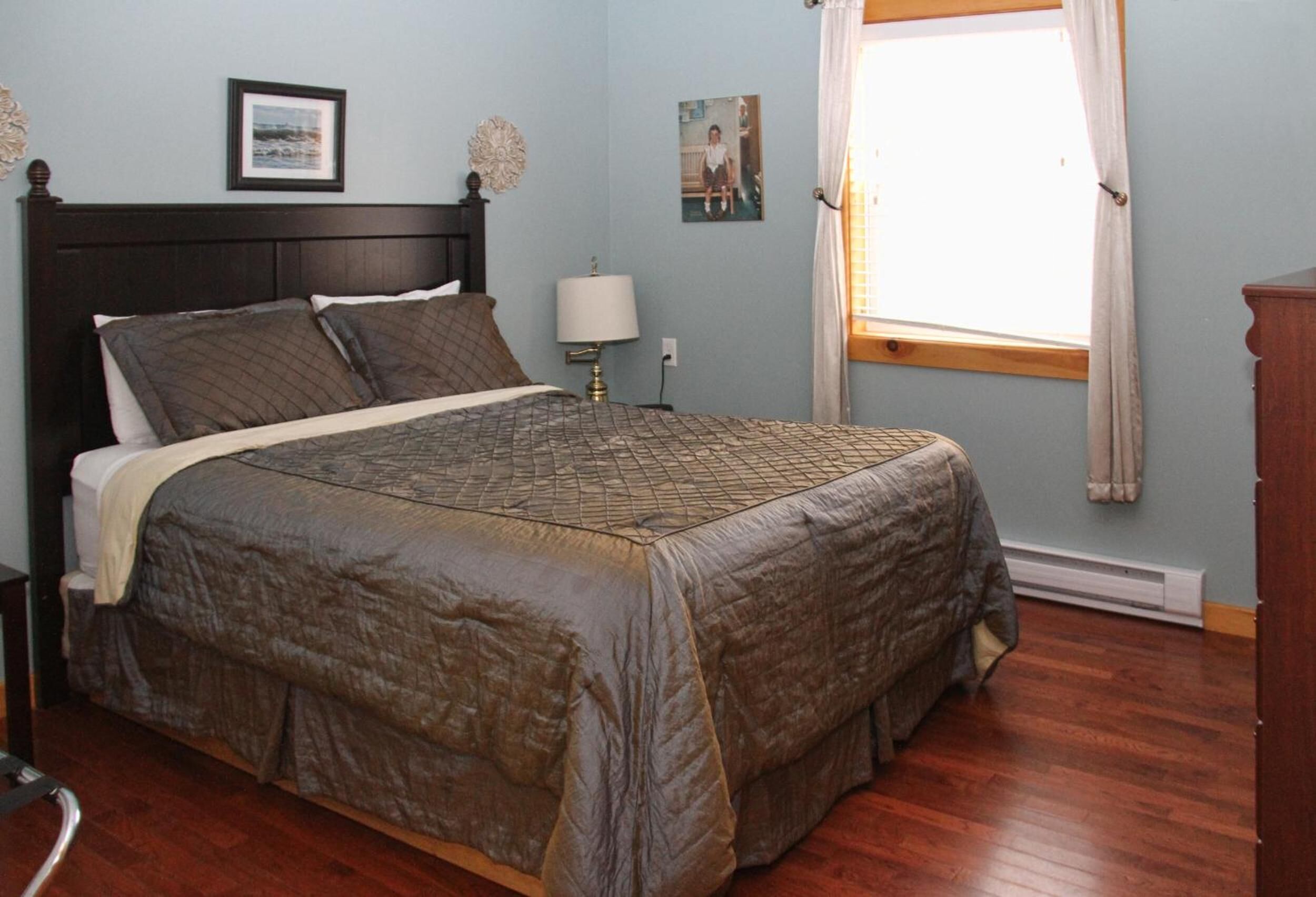 A bedroom with a large bed, a nightstand, a lamp, and a window with curtains.