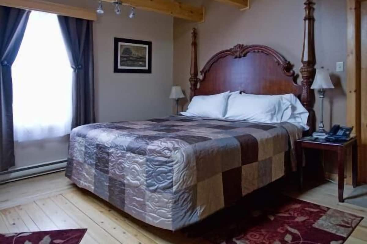 A bedroom with a wooden ceiling, a large bed with a patterned bedspread, two bedside tables, and a nightstand.