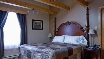A bedroom with a wooden ceiling, a large bed with a patterned bedspread, two bedside tables, and a nightstand.
