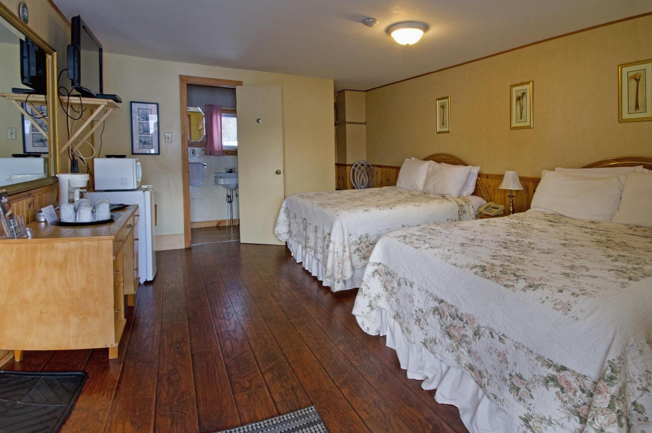 Une chambre d’hôtel avec deux lits, un bureau, un miroir et une porte donnant sur une salle de bain.
