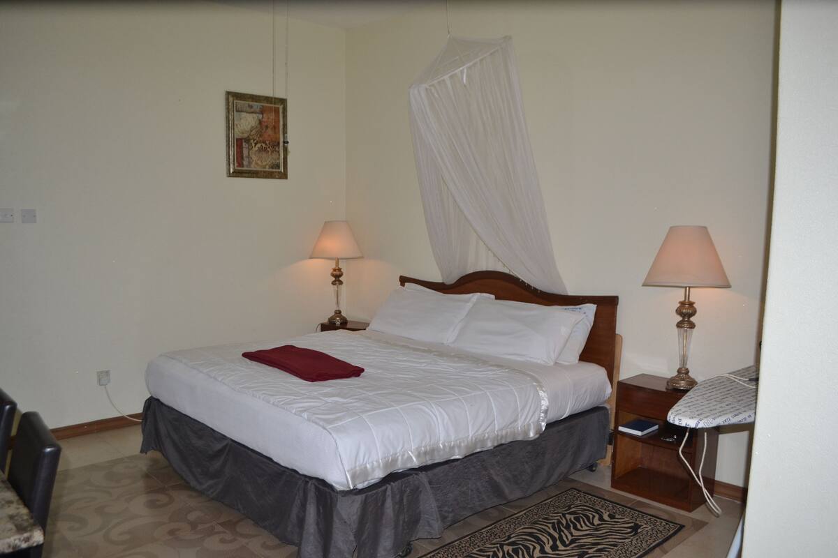 A neatly made bed with a red blanket, two bedside lamps, a wooden nightstand, and a zebra-patterned rug.