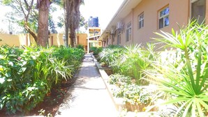 A narrow pathway flanked by lush greenery and a building with multiple windows. - Executive Airport Hotel (Entebbe)