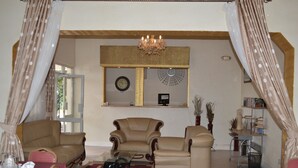 A living room with a glass coffee table, two leather armchairs, a dining table set with plates and glasses, and a chandelier. - Executive Airport Hotel (Entebbe)