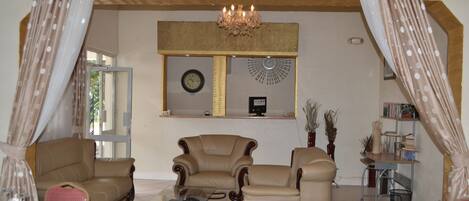 A living room with a glass coffee table, two leather armchairs, a dining table set with plates and glasses, and a chandelier.