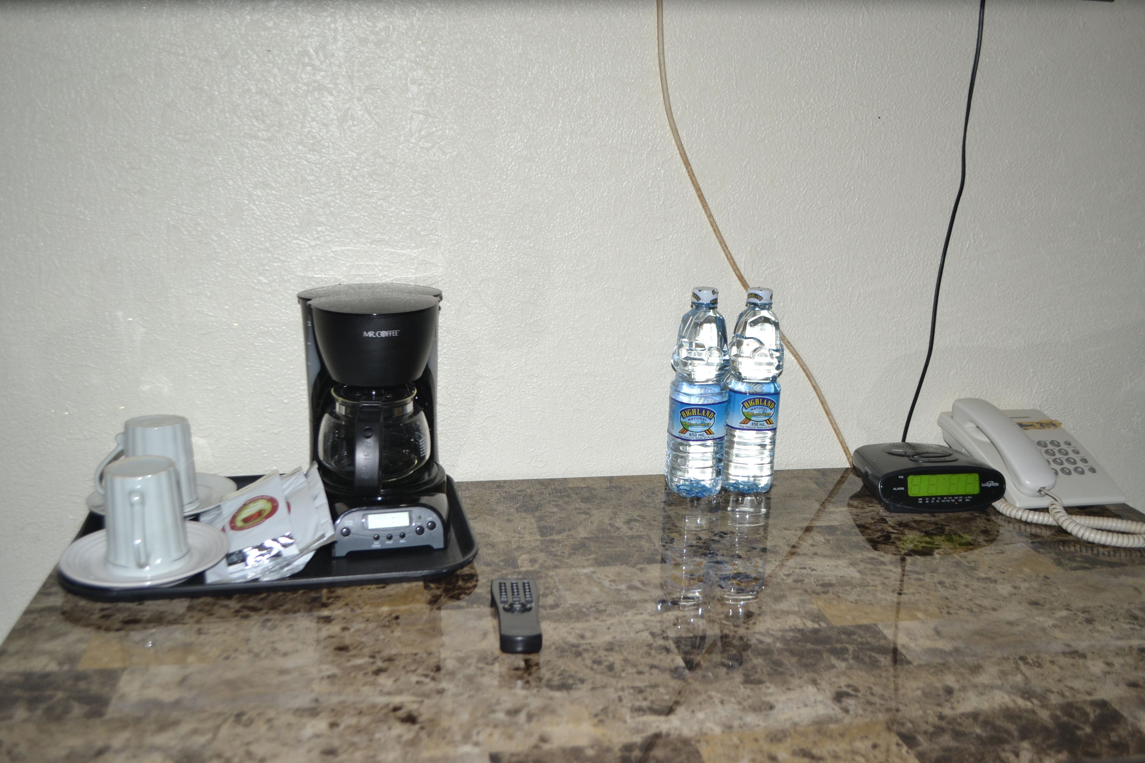 Eine Küchenarbeitsplatte mit einer Kaffeemaschine, zwei Wasserflaschen, einem Telefon und einer Fernbedienung.