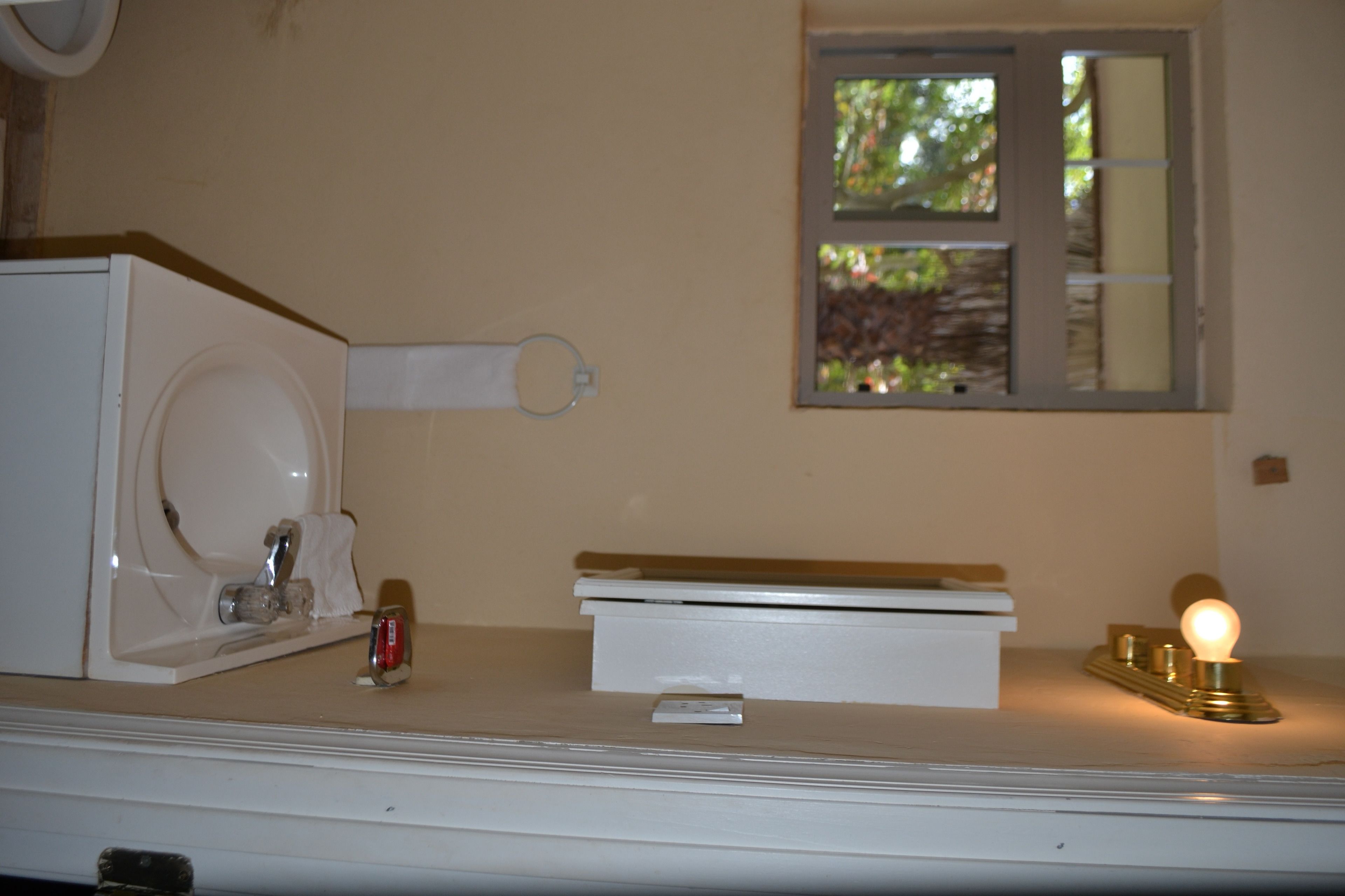 A bathroom with a white sink, a mirror, a window with a view of greenery, and a light fixture on the counter.
