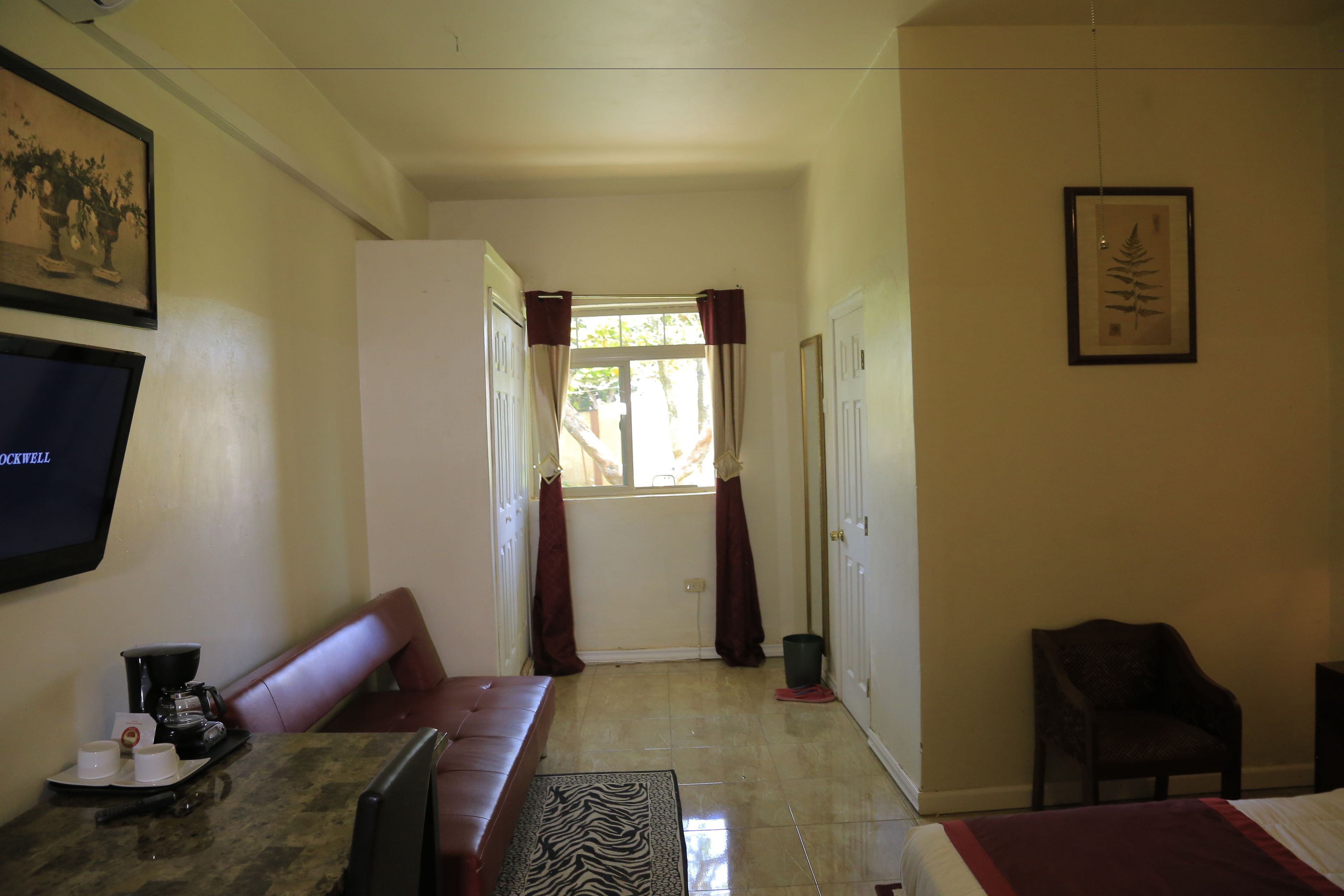 Una habitación de hotel con cama, sofá, espacio para café, televisión y ventana con cortinas.