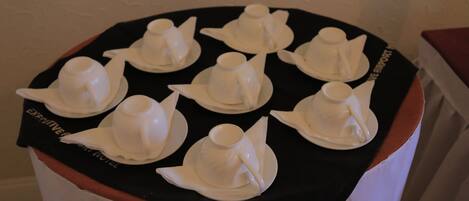 A table with white teapots and saucers arranged on a black cloth.