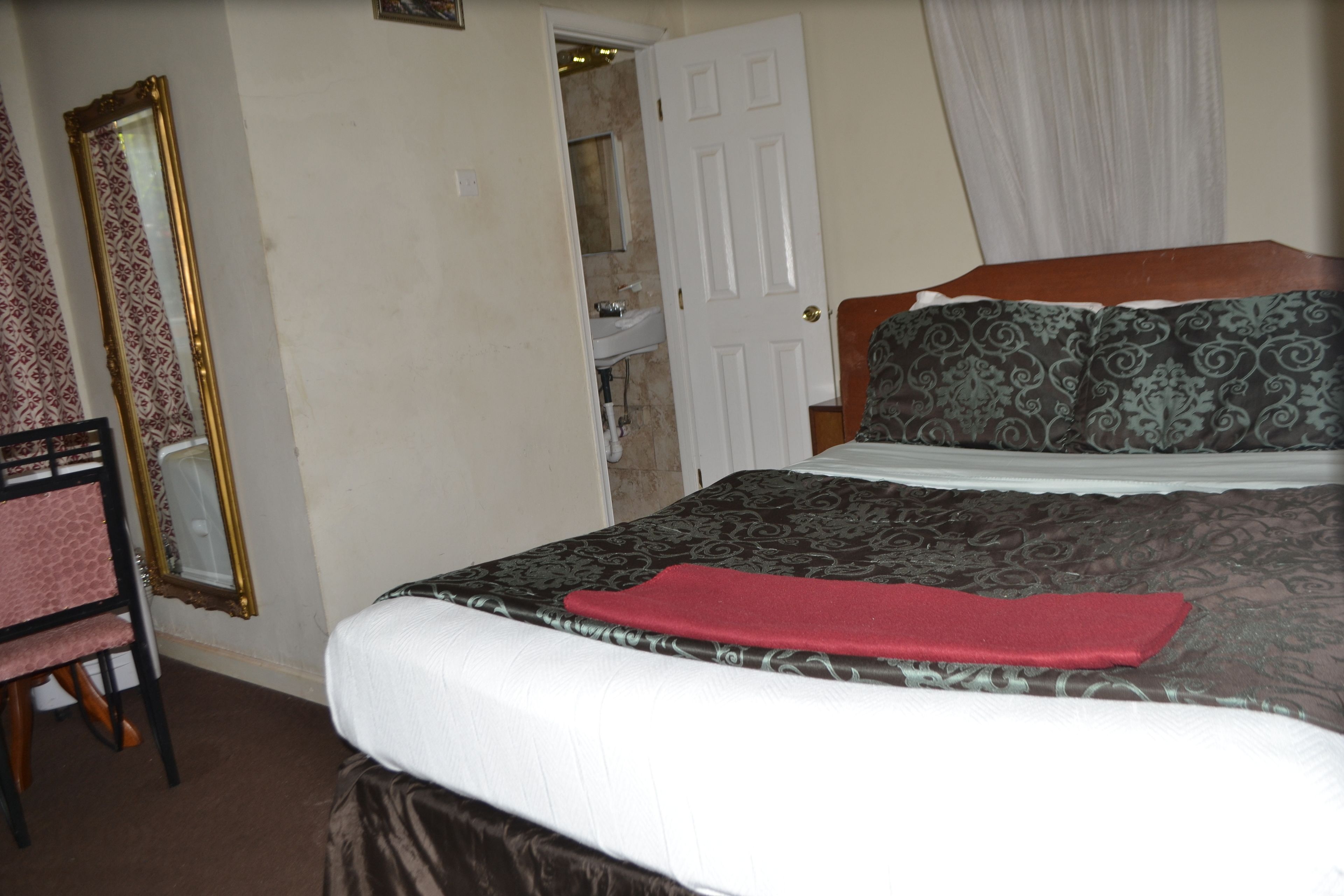 A bedroom with a bed, a mirror, a chair, and a door leading to a bathroom.