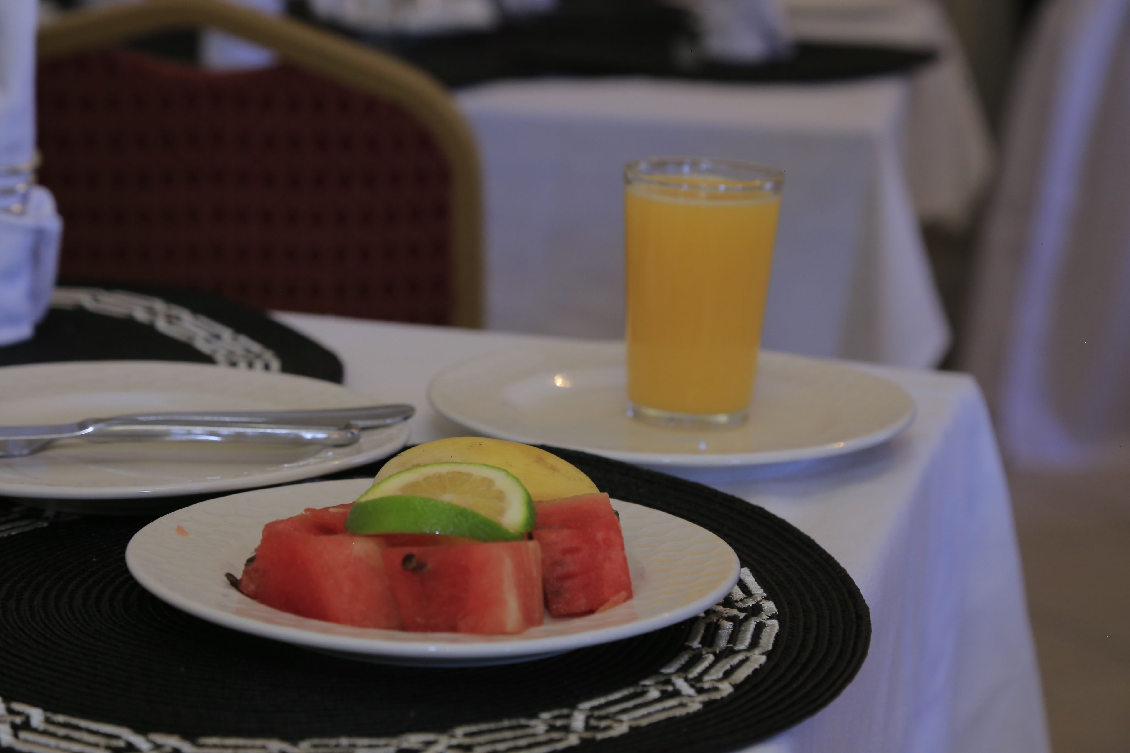A table with a plate of watermelon and a glass of orange juice.