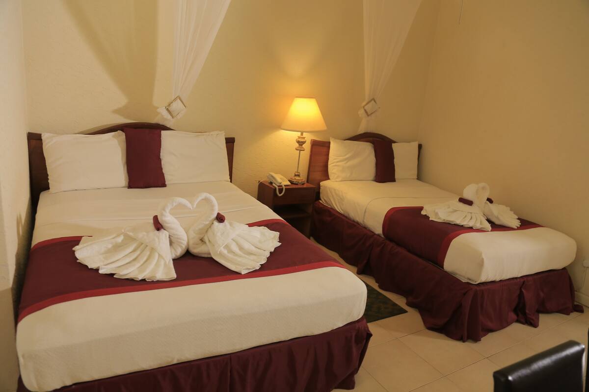 A hotel room with two beds, each with a red bedspread and white pillows. There is a nightstand with a lamp between the beds.
