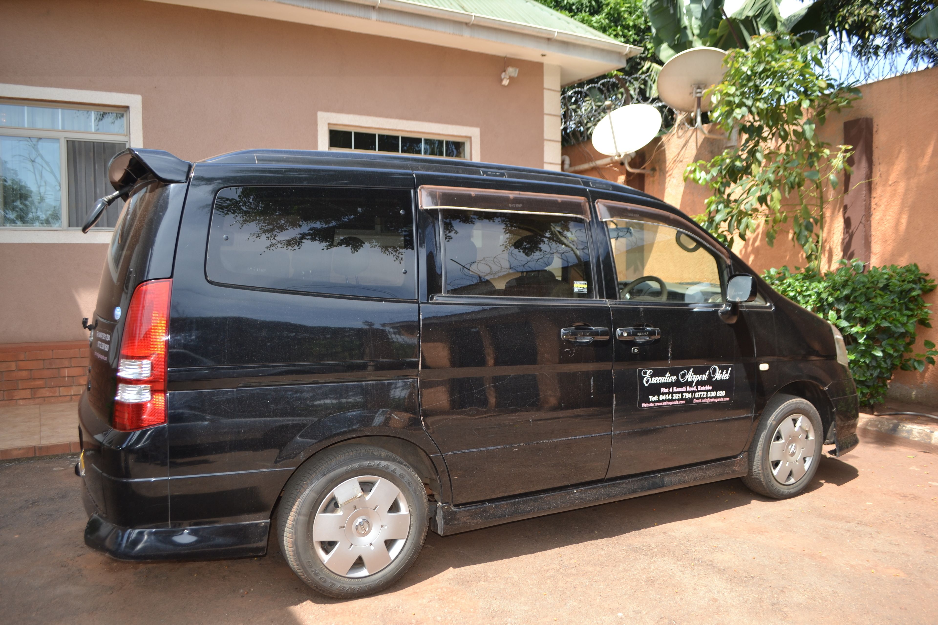 A black van parked in front of a building with a satellite dish and a window.
