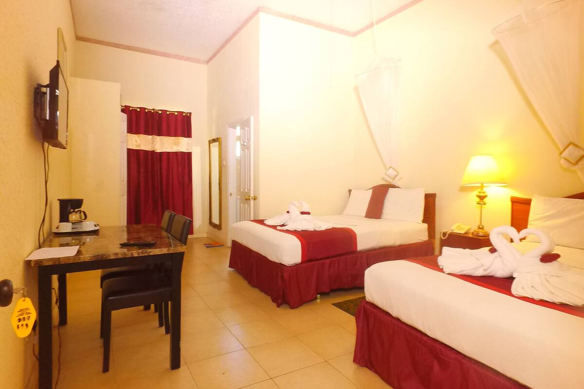 A hotel room with two beds, a desk, a chair, a TV, and a lamp.