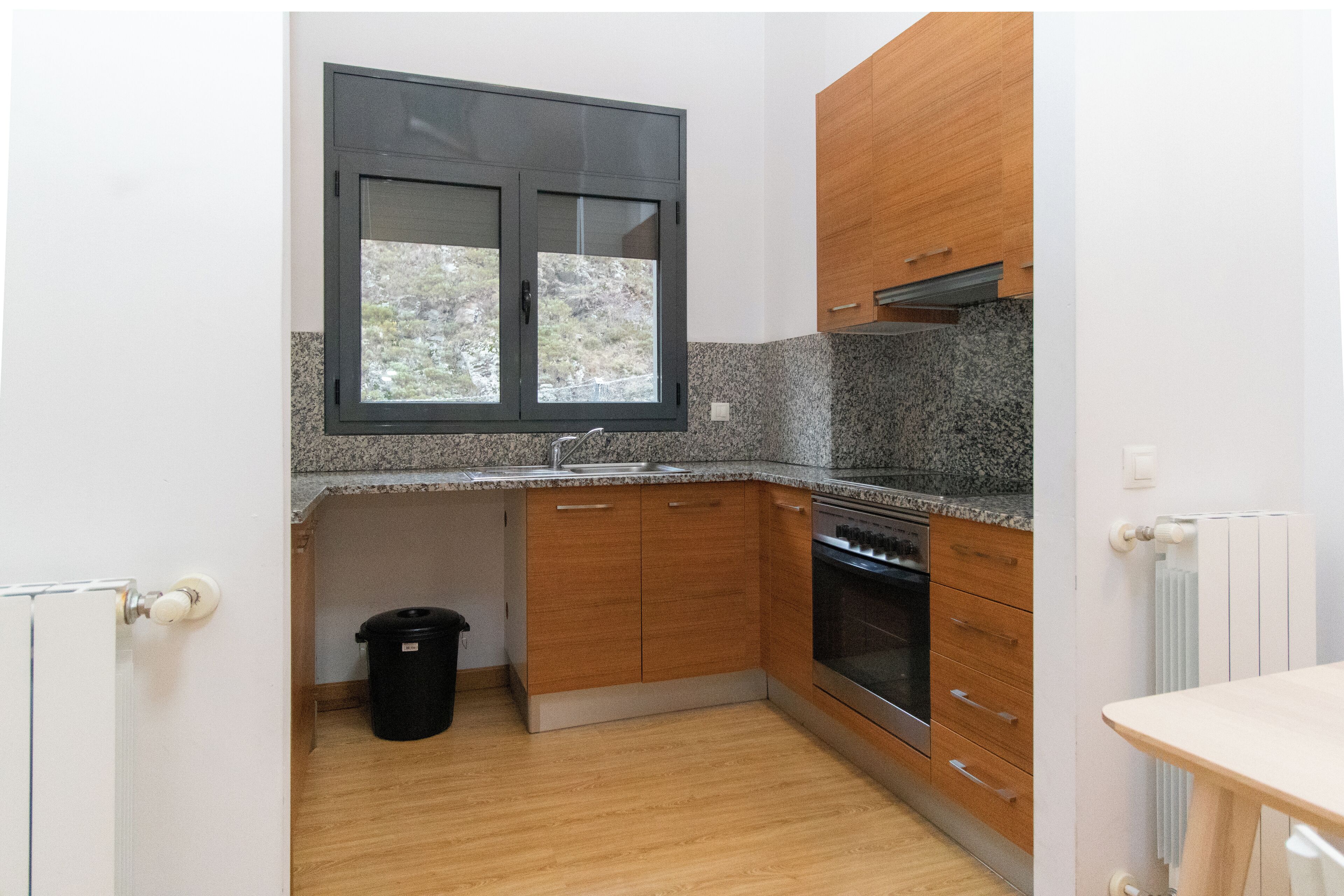 Una cocina compacta con encimeras de granito, armarios de madera, horno integrado y una ventana sobre el fregadero.