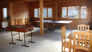 A wooden-floored room with a foosball table, chairs, and a table with a red tablecloth. - Apartamentos La Pleta Incles Suites 3000 (Soldeu)