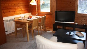 A cozy cabin interior with a wooden dining table set for four, a television on a stand, and a sofa in the foreground. - Apartamentos La Pleta Incles Suites 3000 (Soldeu)