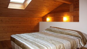 A bedroom with a sloped ceiling, wooden walls, a skylight, and a bed with striped bedding. - Apartamentos La Pleta Incles Suites 3000 (Soldeu)