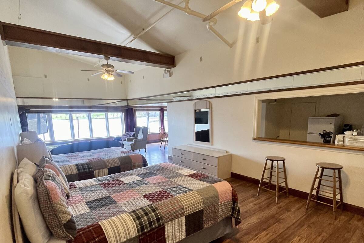 Una habitación amplia con una cama grande, ventilador de techo, kitchenette y vistas al exterior.