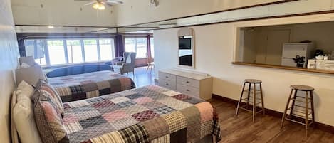 A spacious room with a large bed, a ceiling fan, a kitchenette, and a view of the outdoors.