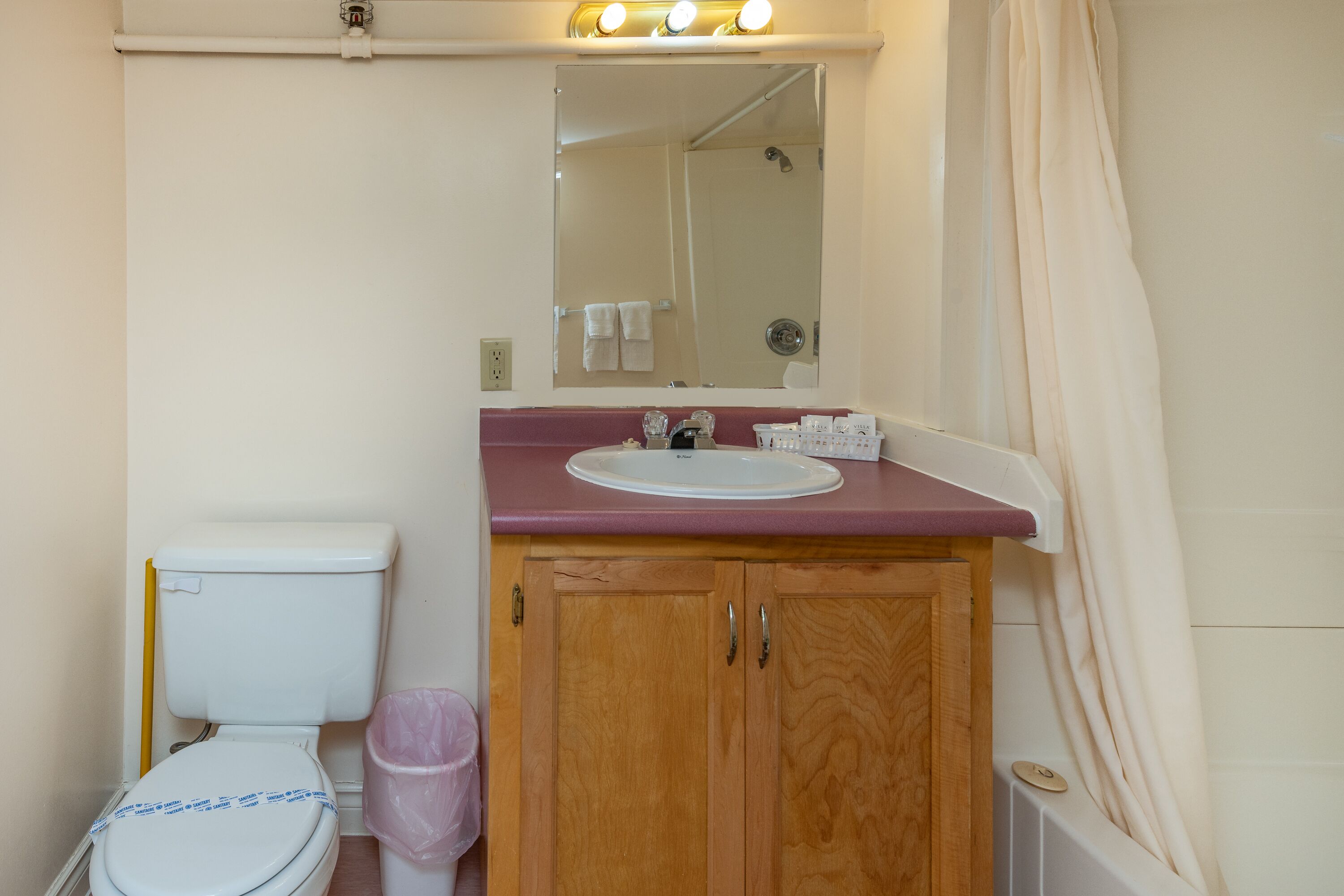 A bathroom with a white toilet, wooden cabinets, a pink sink, and a mirror above the sink.