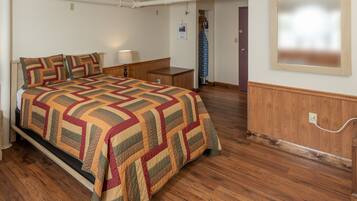 A bedroom with a bed, bedside table, lamp, and a wooden dresser.
