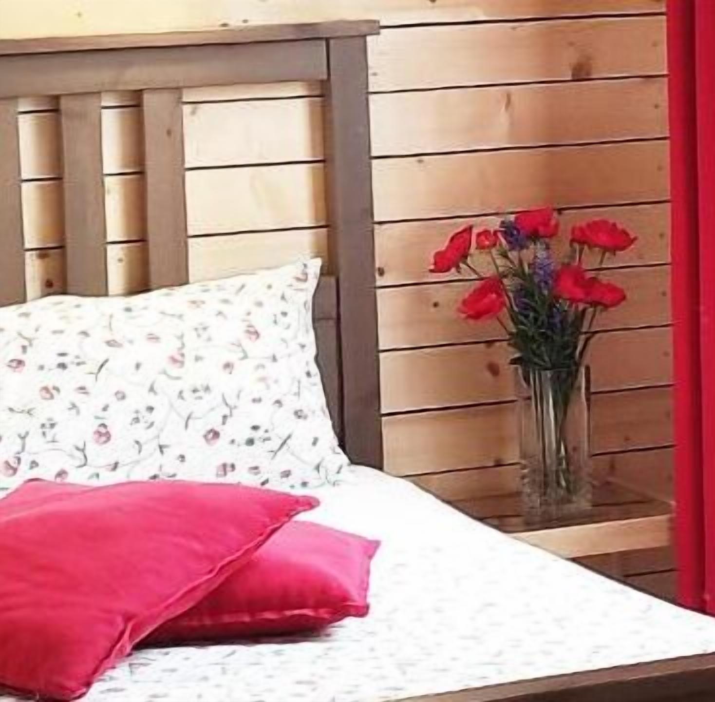 A bed with a floral pillow and a red pillow, a vase with red flowers, and wooden paneling on the wall.