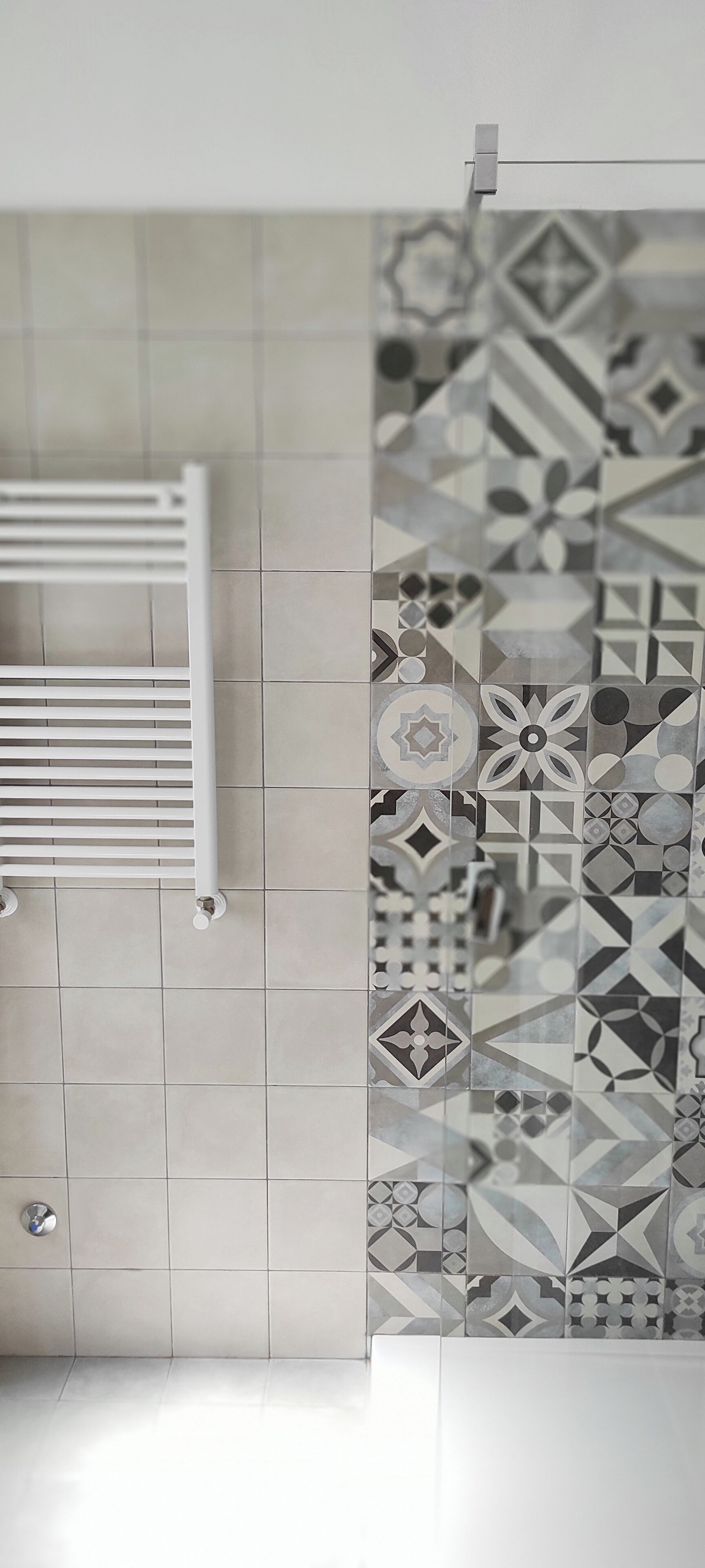 A bathroom with a white towel rack, a tiled wall with geometric patterns, and a shower area.
