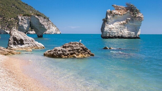 A coastal landscape with clear blue waters, rocky formations, and a sandy beach. - Apulia Bed & Breakfast (Mattinata)