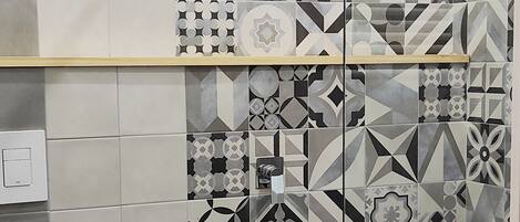 Une salle de bain avec douche, toilettes et un mur recouvert de carreaux aux motifs géométriques.