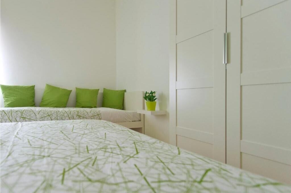 Un dormitorio con cama, almohadas verdes, una planta en la mesita de noche y un armario.