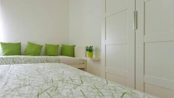 Un dormitorio con cama, almohadas verdes, una planta en la mesita de noche y un armario.