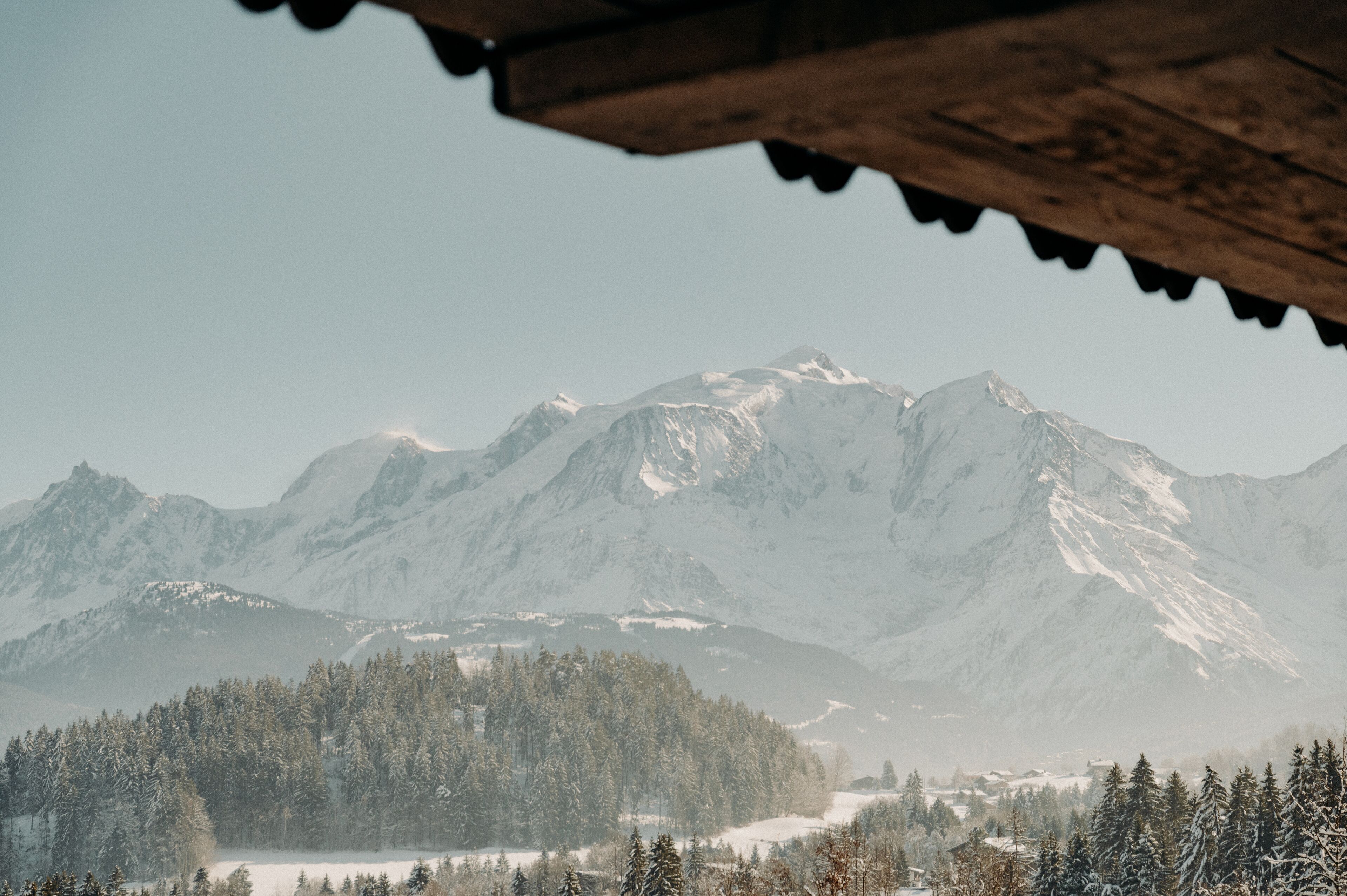 Paisagem montanhosa com picos cobertos de neve e um vale arborizado.