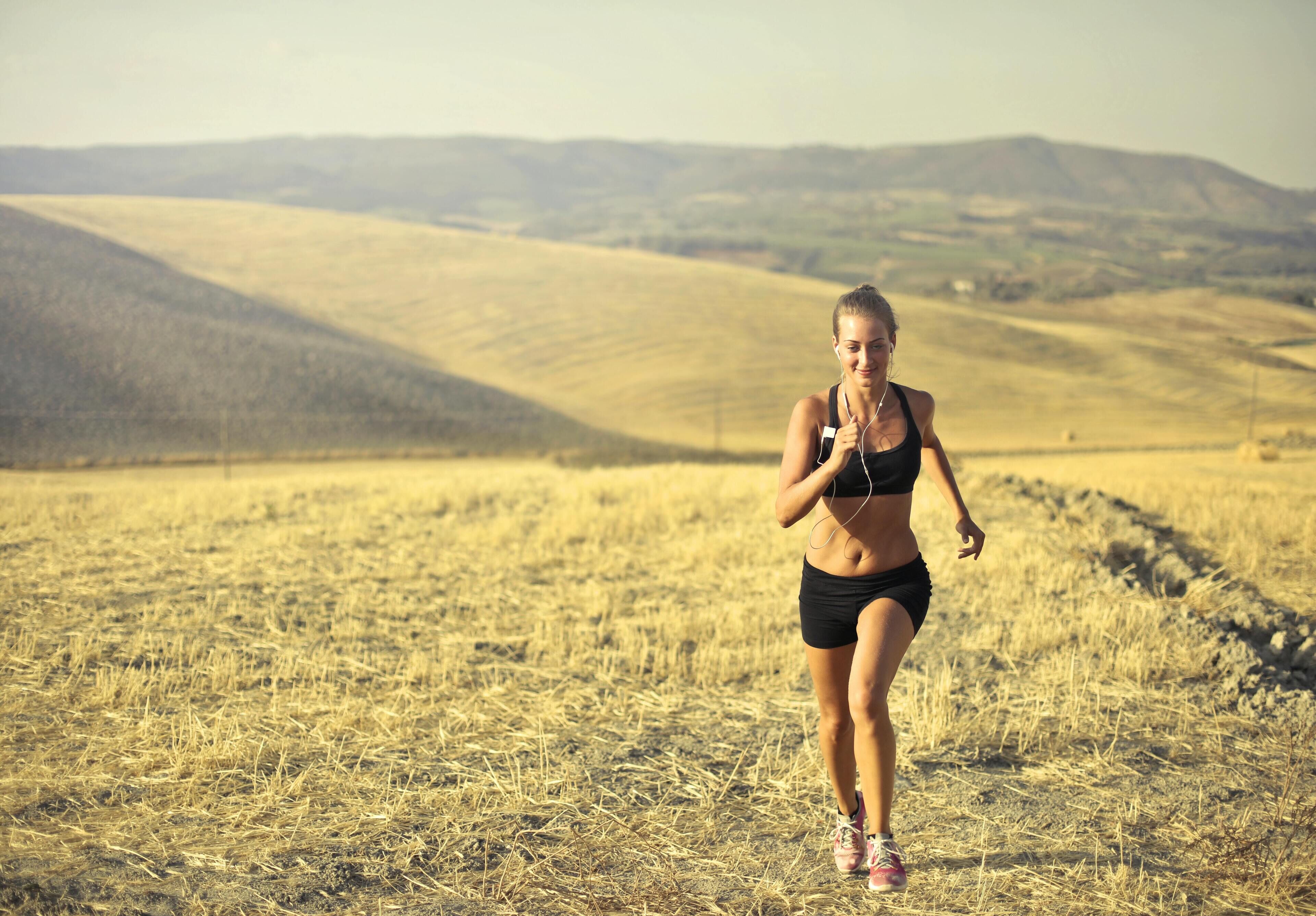 A person jogging in a dry, grassy field with rolling hills in the background.