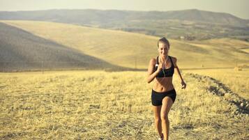 A person jogging in a dry, grassy field with rolling hills in the background.