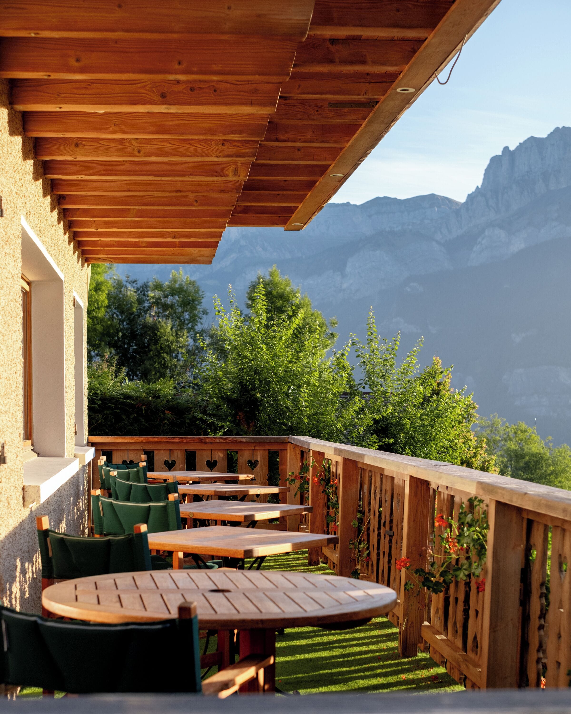 A wooden deck with tables and chairs, overlooking a mountainous landscape.