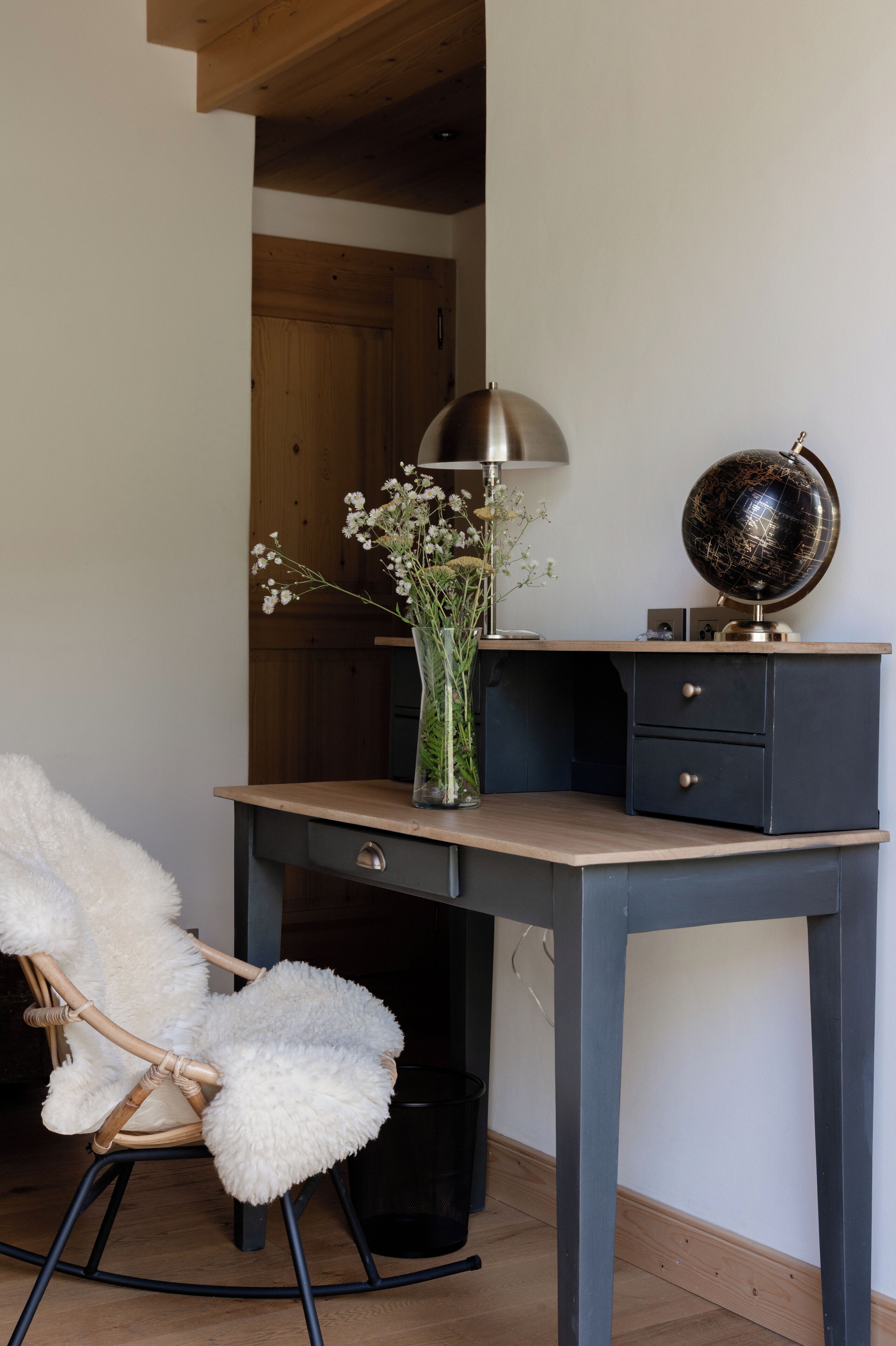 Un espacio de trabajo con escritorio, silla, globo terráqueo, lámpara y flores.
