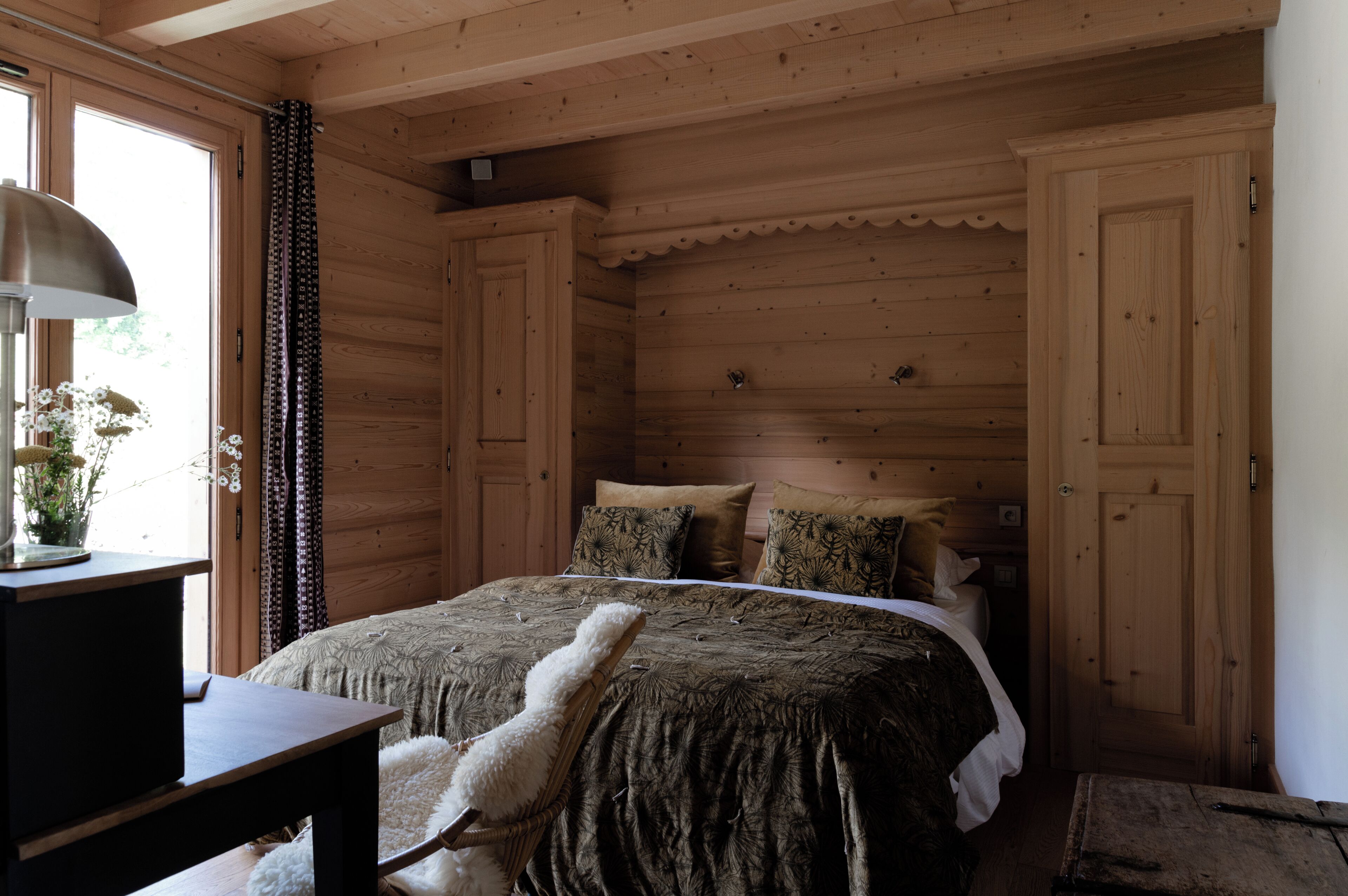 Dormitorio de cabaña de madera con una cama, un escritorio y una silla.