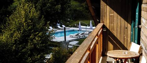 A wooden deck with a pool and lounge chairs, surrounded by trees.