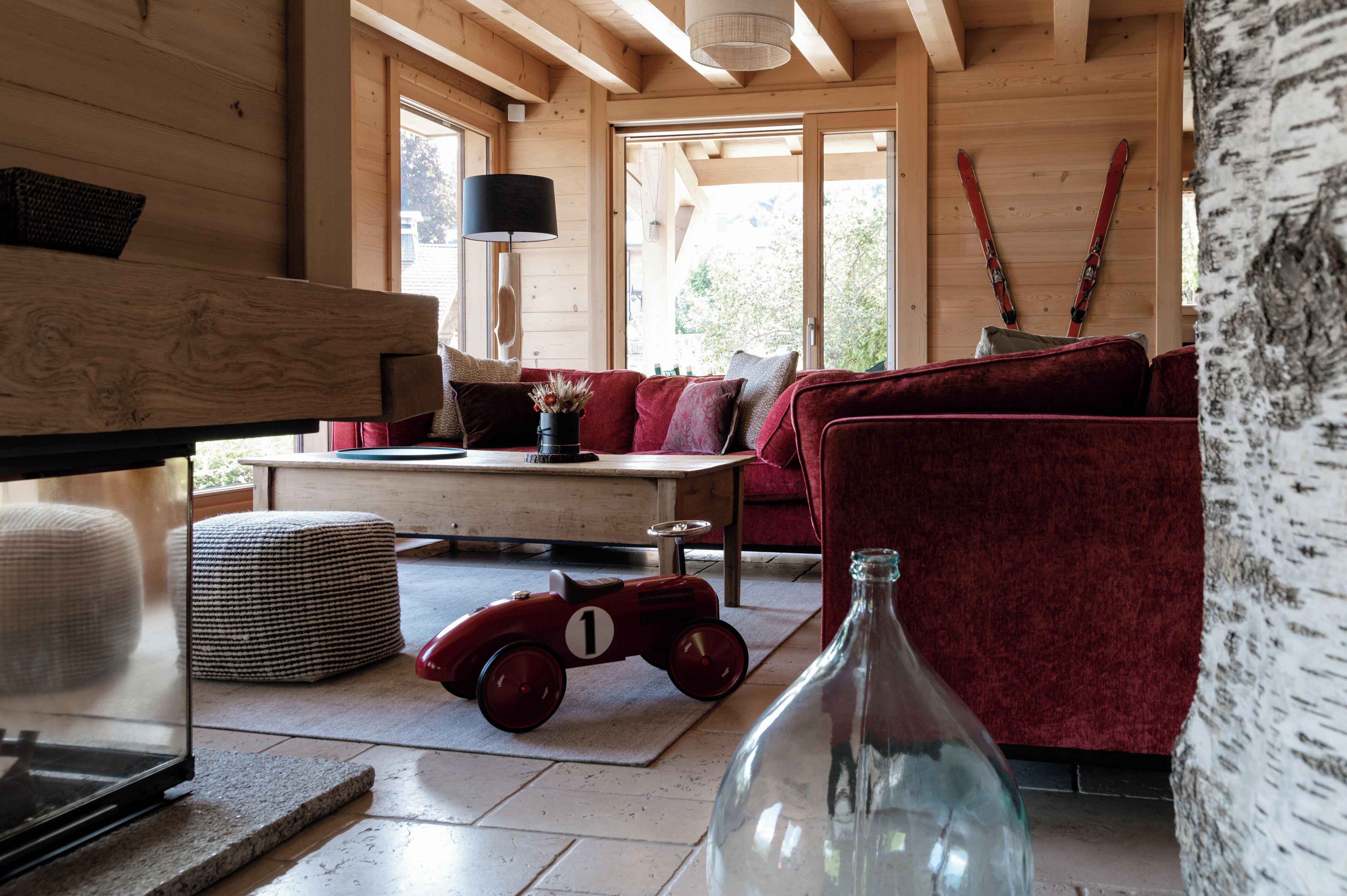 Un interior de madera acogedor con un sofá rojo, un pequeño coche de juguete rojo y una botella de vidrio sobre una mesa.