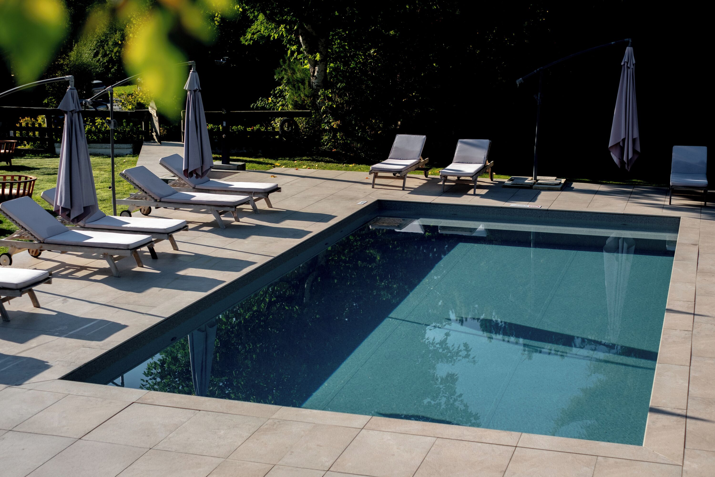 A rectangular swimming pool with a tiled deck, surrounded by lounge chairs and umbrellas.